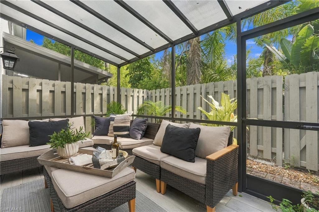 Screened patio with wicker sectional seating, a cushioned ottoman, and tropical greenery.