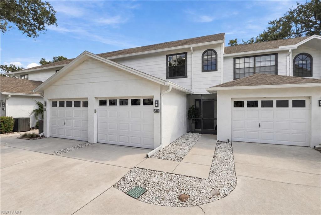 Two-story white townhouse with arched windows, multiple garage doors, and a stone-bordered entry walkway.