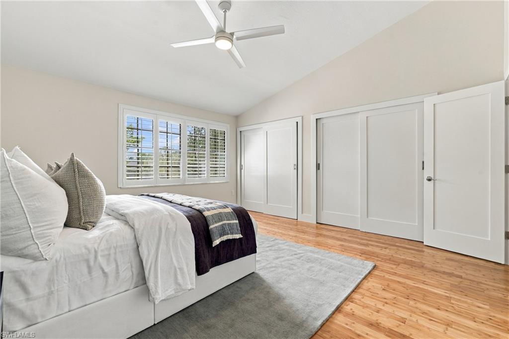 Bedroom with plantation-shuttered windows, a white bed, wood floors, and large closet doors.