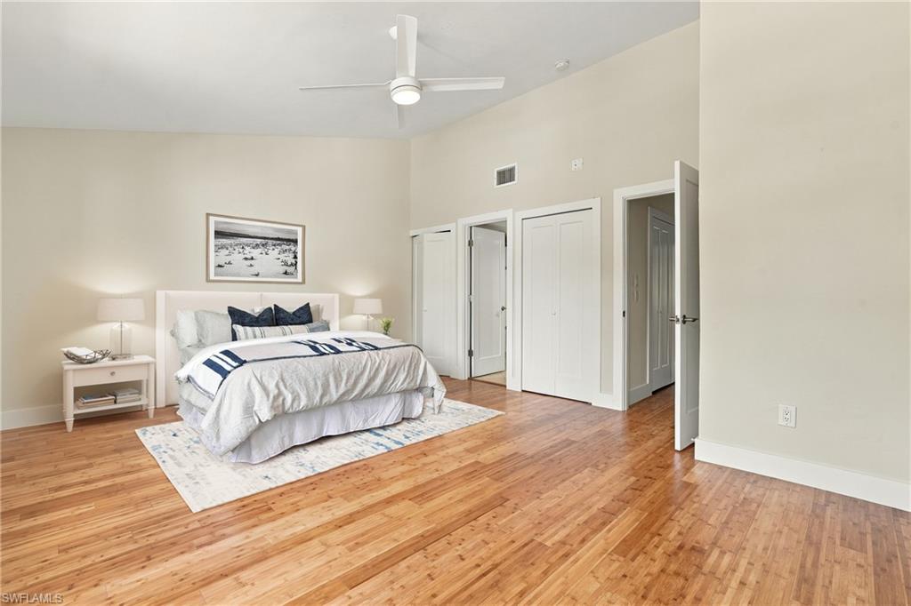 Staged bedroom with a king-size bed, navy accents, hardwood floors, and a white ceiling fan.