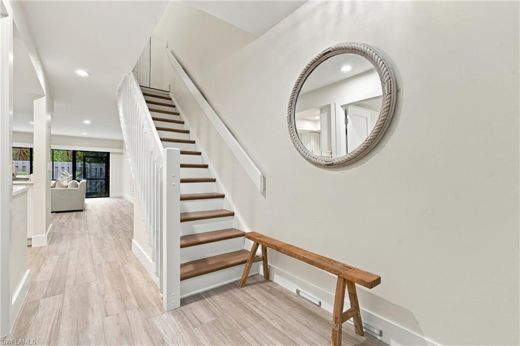 White staircase with dark wood treads beside a round mirror and wooden bench.