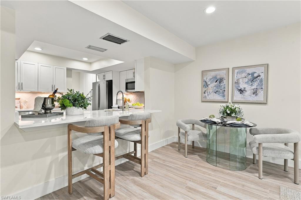 Kitchen and dining area with white cabinets, breakfast counter, and round glass table.