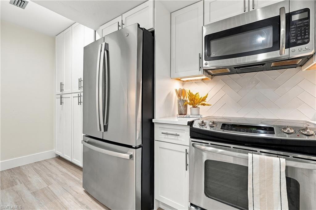 Kitchen with stainless steel appliances, white cabinetry, and a herringbone tile backsplash.