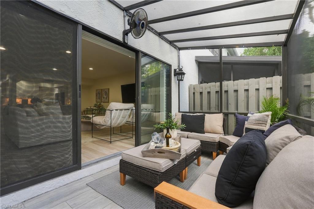 Covered lanai with cushioned wicker seating beside sliding glass doors and a privacy fence.