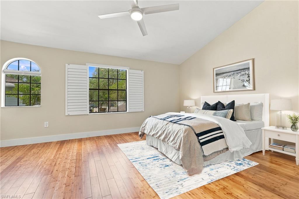 Staged bedroom with a white bed, navy accents, hardwood floors, and shuttered windows.