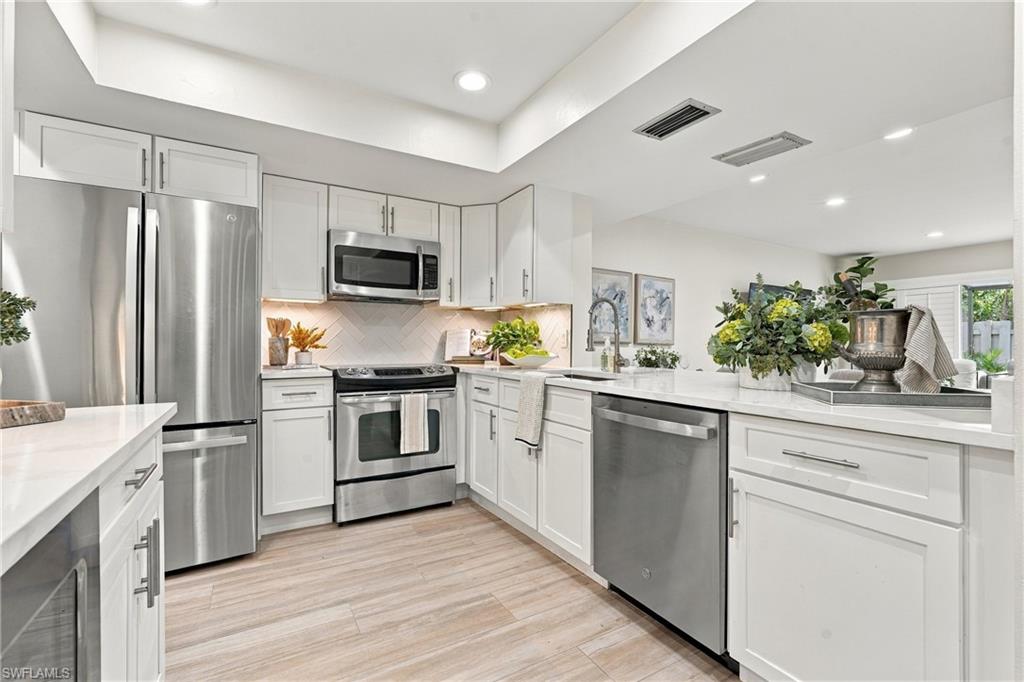 Bright kitchen with white cabinetry, stainless steel appliances, and a sink island.