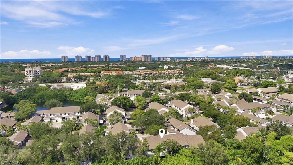 Aerial view of a Naples neighborhood, with a location pin, distant high-rises, and the Gulf on the horizon.