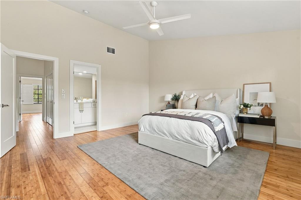 Bedroom with a white bed on a gray rug, hardwood floors, and a ceiling fan.