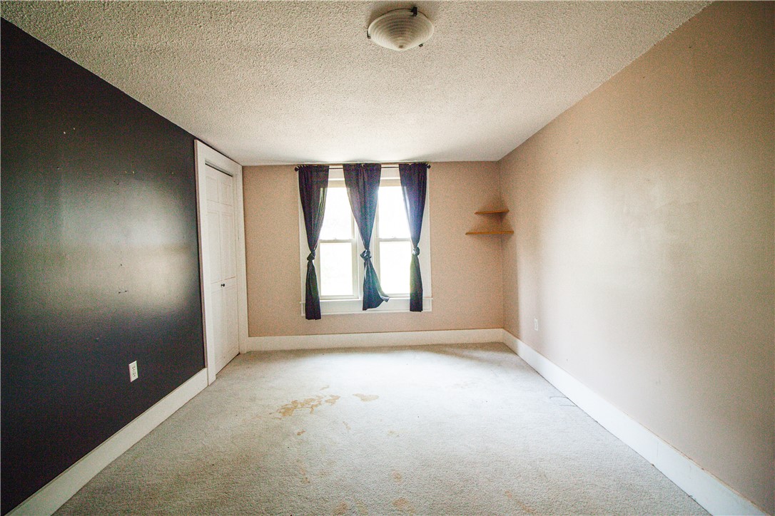 Vacant bedroom with a dark accent wall, curtained window, and stained carpet.