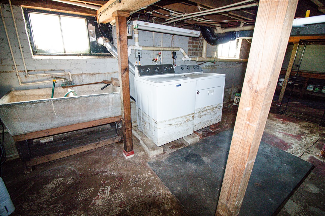 Basement laundry area with a white washer and dryer, exposed pipes, and a utility sink.