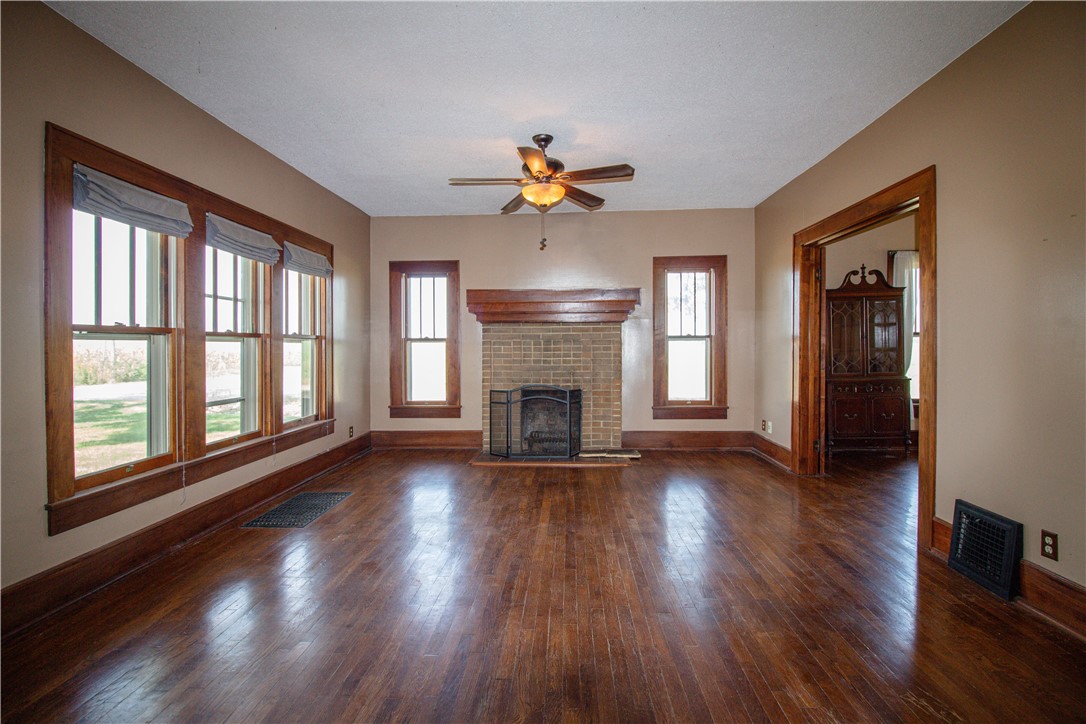 Empty living room with hardwood floors, brick fireplace, and tall wood-trimmed windows.