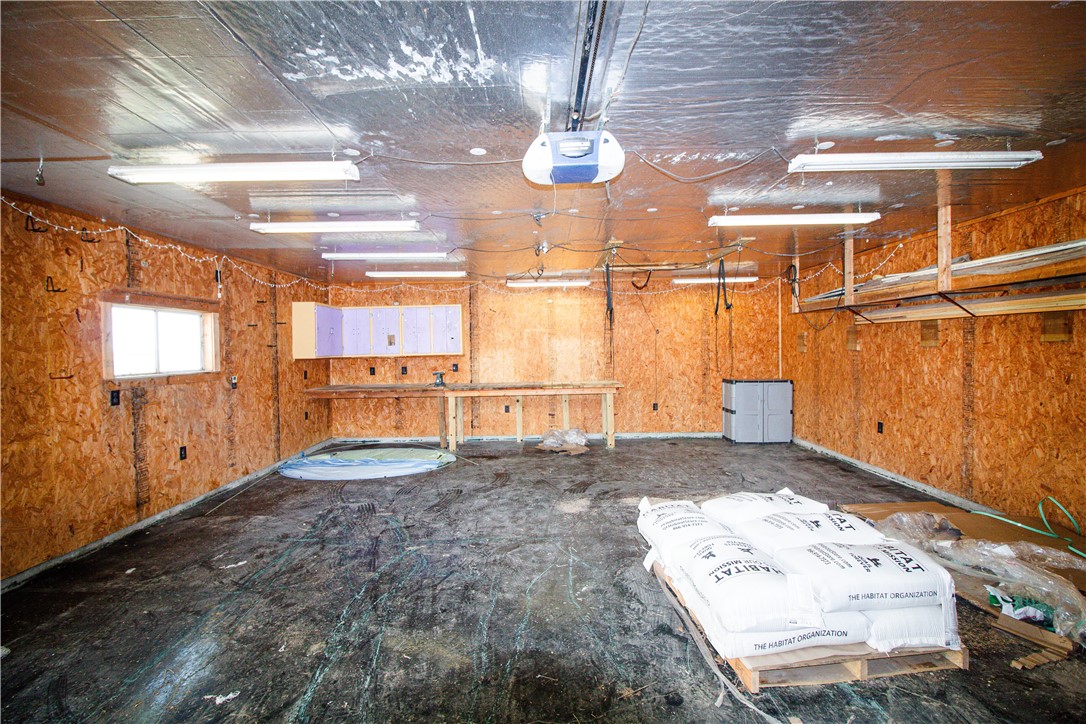 Garage workshop with exposed OSB walls, a workbench, fluorescent lights, and bags stacked on a pallet.