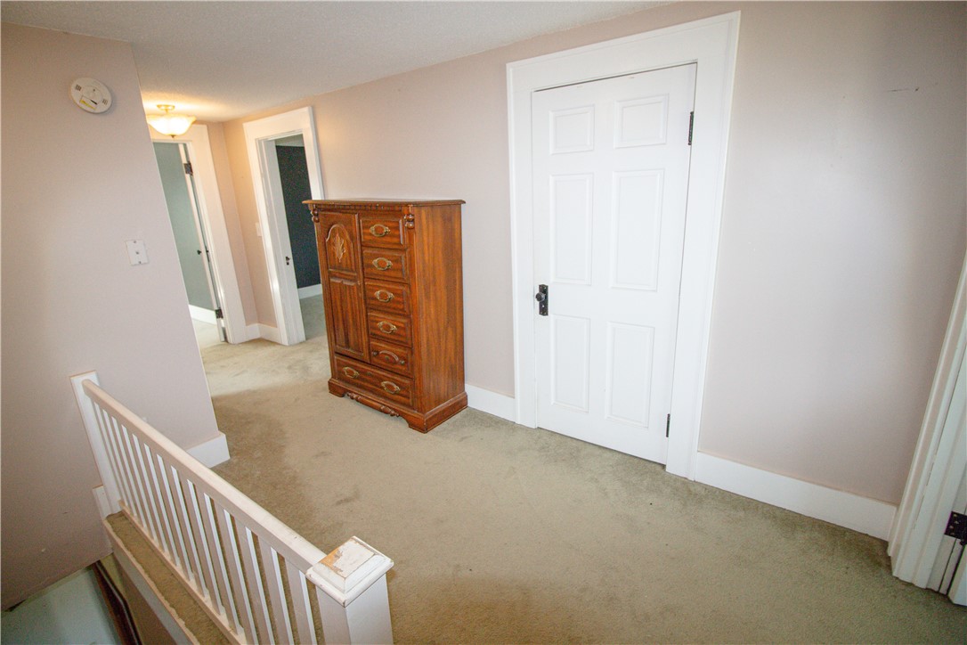 Carpeted upstairs landing with a wooden dresser beside a white door and stair railing.