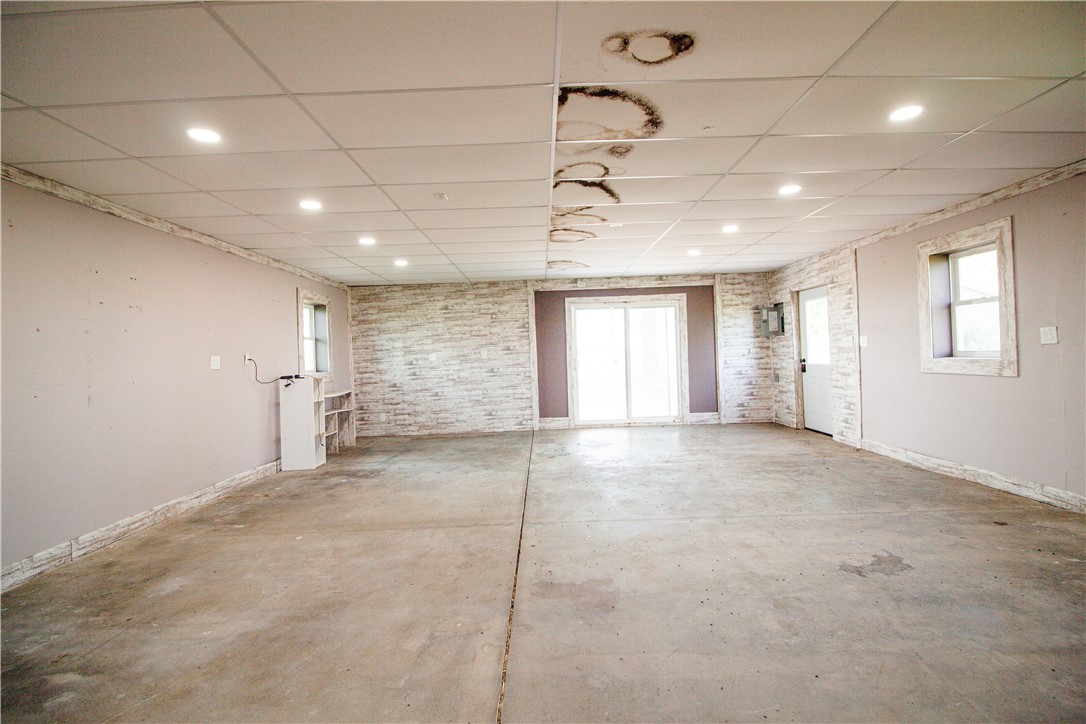 Vacant open room with a concrete floor, stained ceiling tiles, and sliding glass doors.