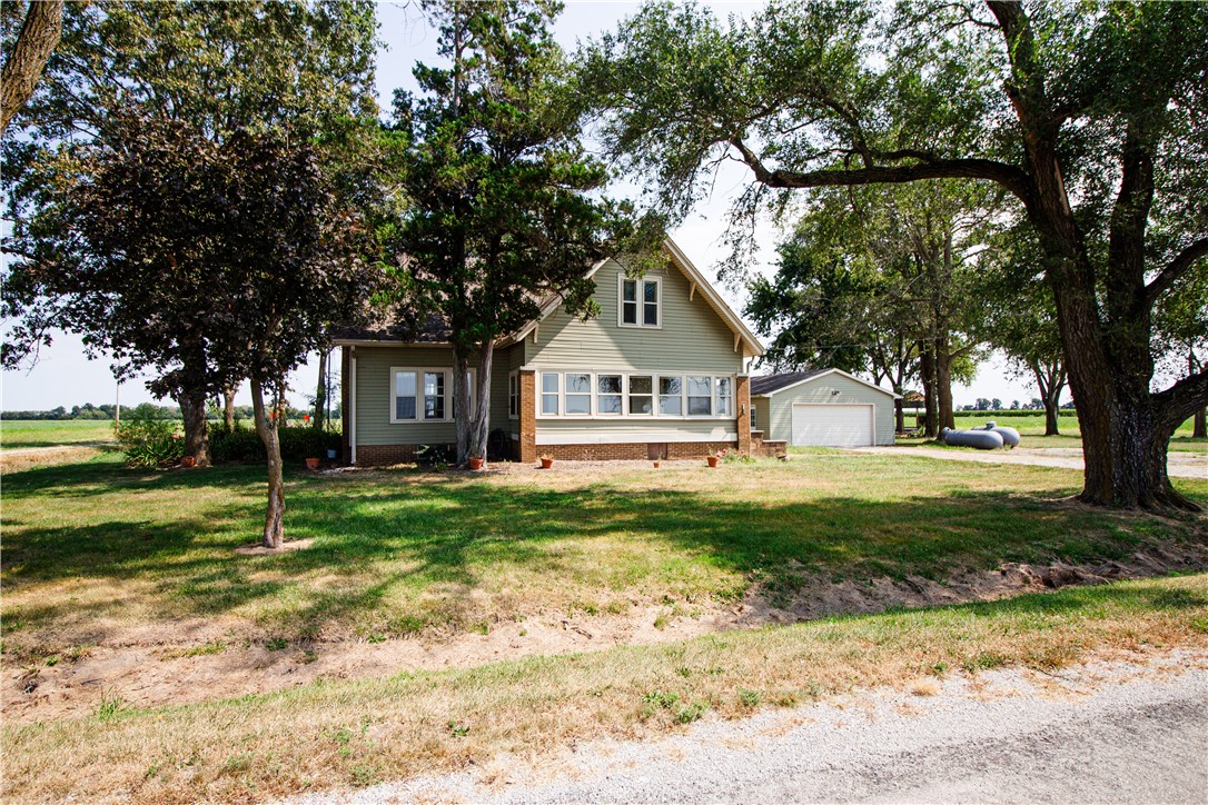Rural house shaded by mature trees, with a detached garage and propane tanks nearby.