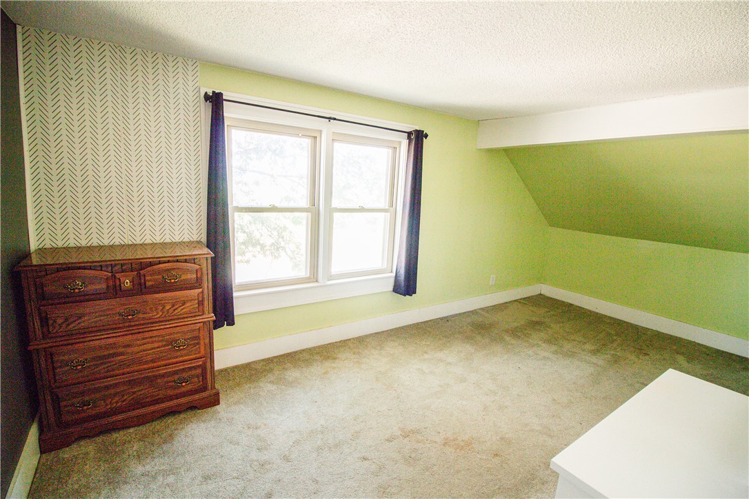 Carpeted bedroom with pale green walls, paired windows, a sloped ceiling, and a wooden dresser.