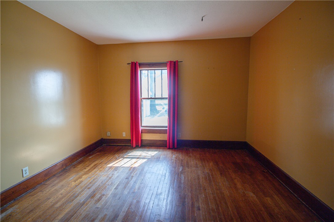 Empty room with hardwood floors, brown walls, and a window framed by red curtains.