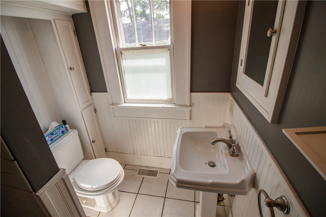 Bathroom with a white pedestal sink, toilet, tiled floor, and beadboard wainscoting.
