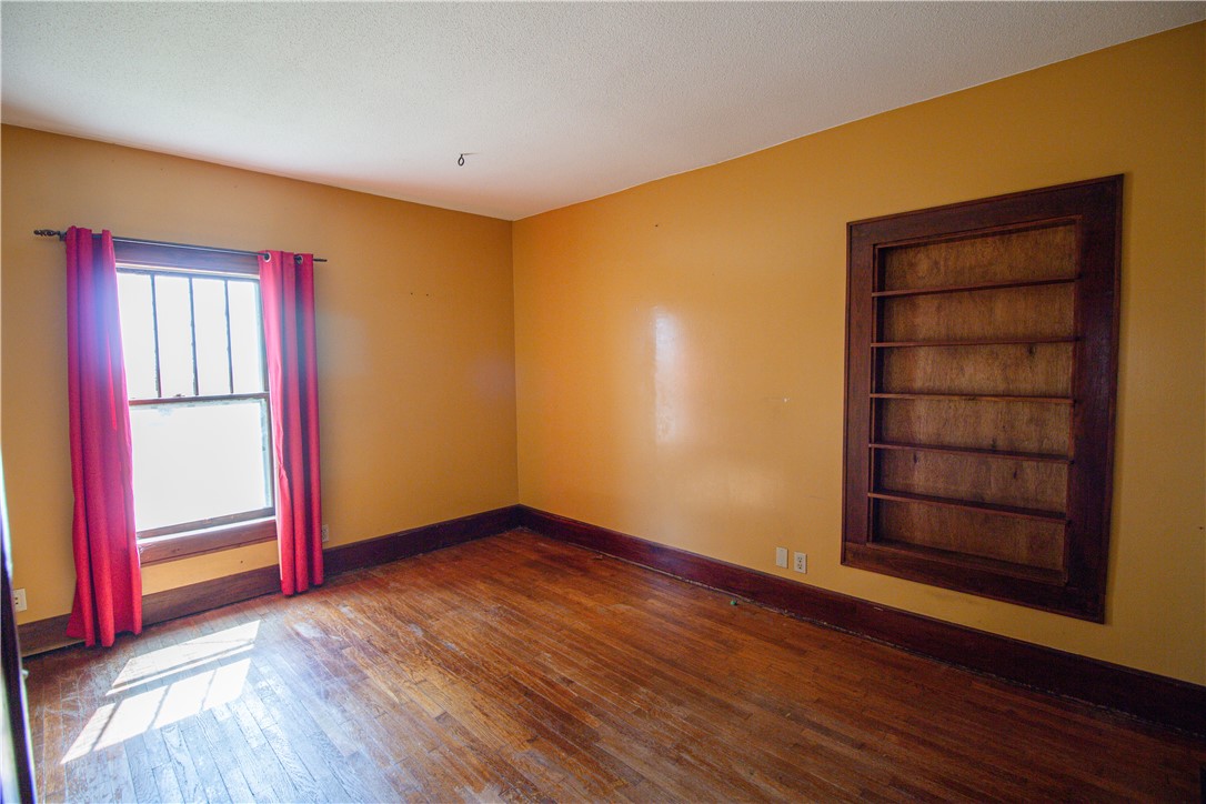 Empty room with red curtains, polished wood floors, and a built-in bookshelf.