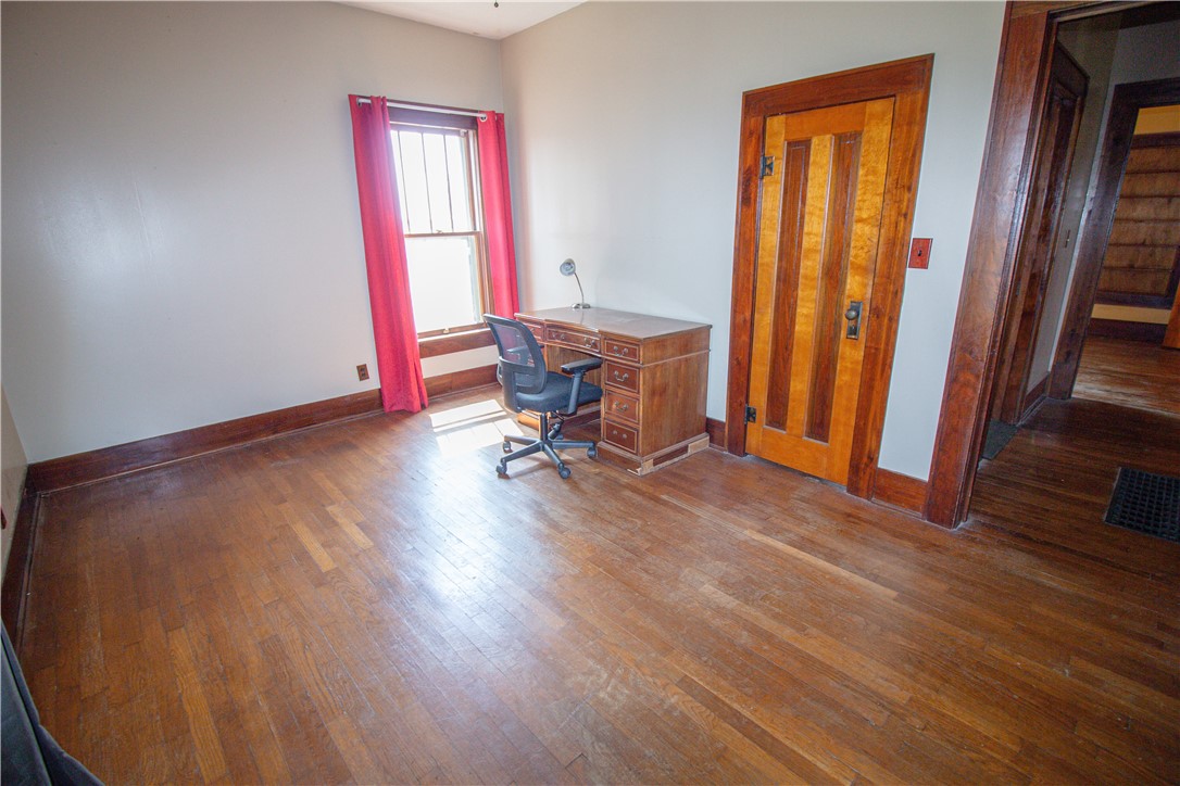 Home office with hardwood floors, a wooden desk, red curtains, and a paneled door.