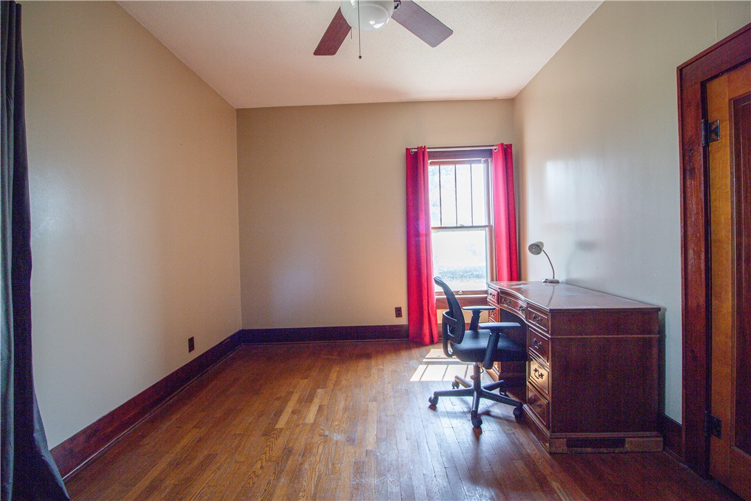 Home office with a dark wood desk, hardwood floors, and red curtains framing the window.