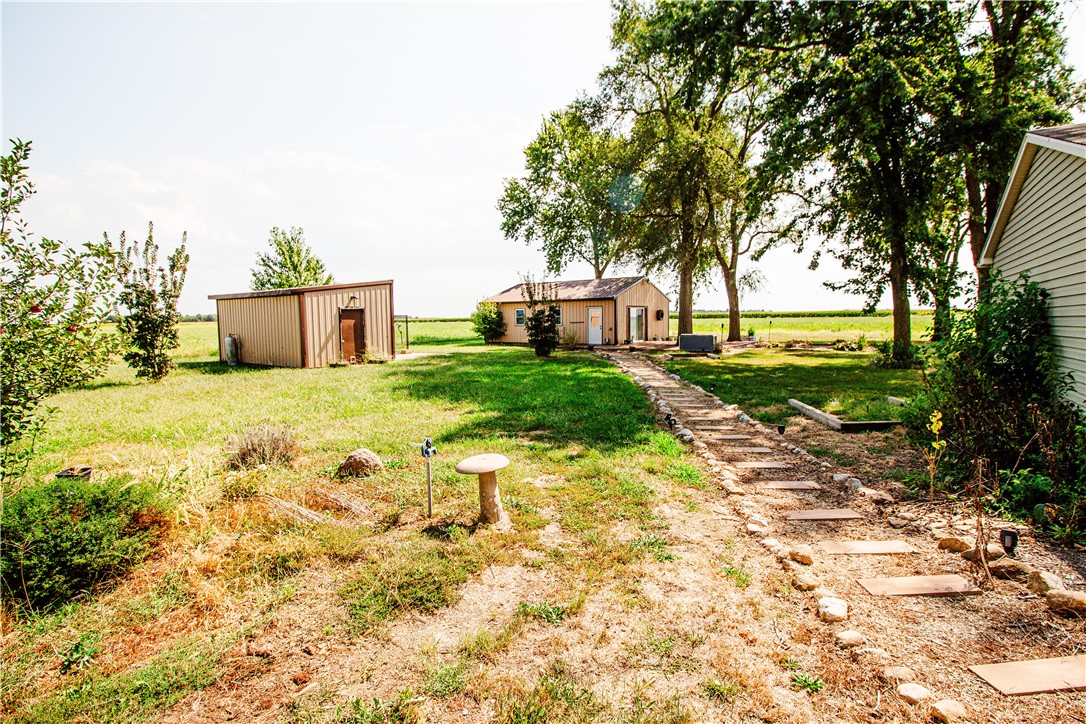 Rural yard with a stepping-stone path, two outbuildings, mature trees, and open fields.