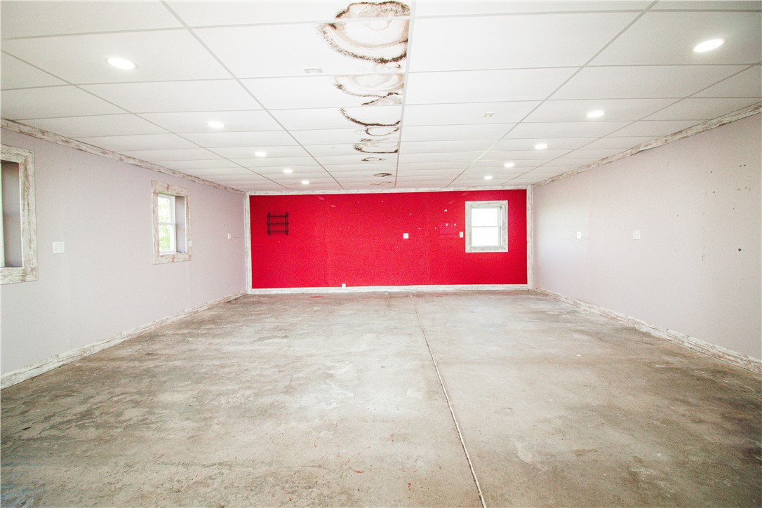 Vacant concrete-floored room with a red end wall and water-stained drop ceiling.