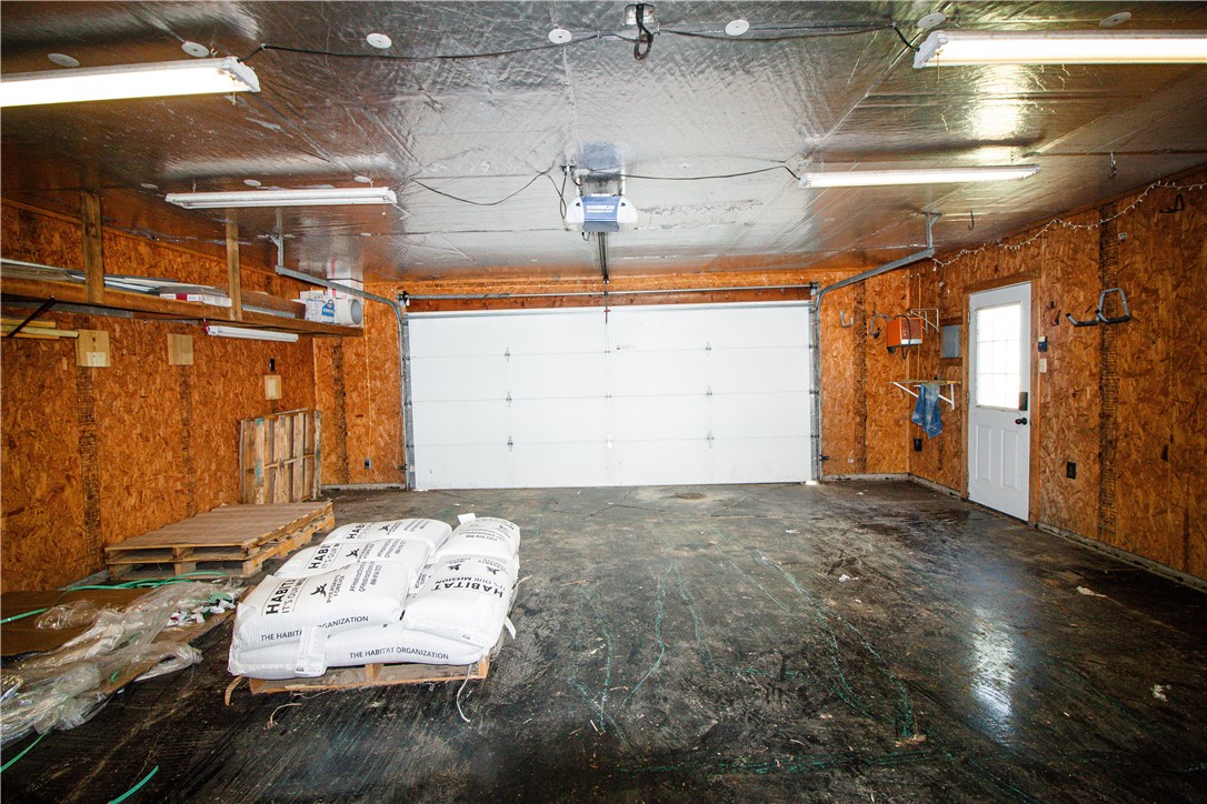Spacious garage with a large white overhead door, exposed wood-chip walls, and bags stacked on a pallet.