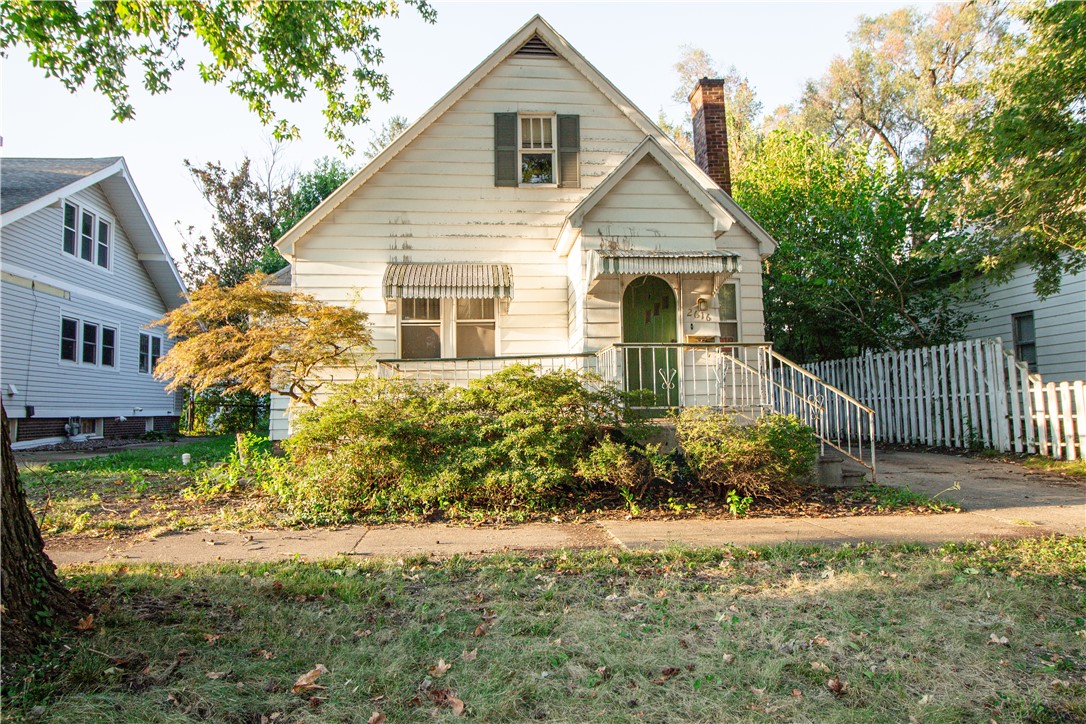 White gable-front house with a covered porch, striped awnings, and a white picket fence.