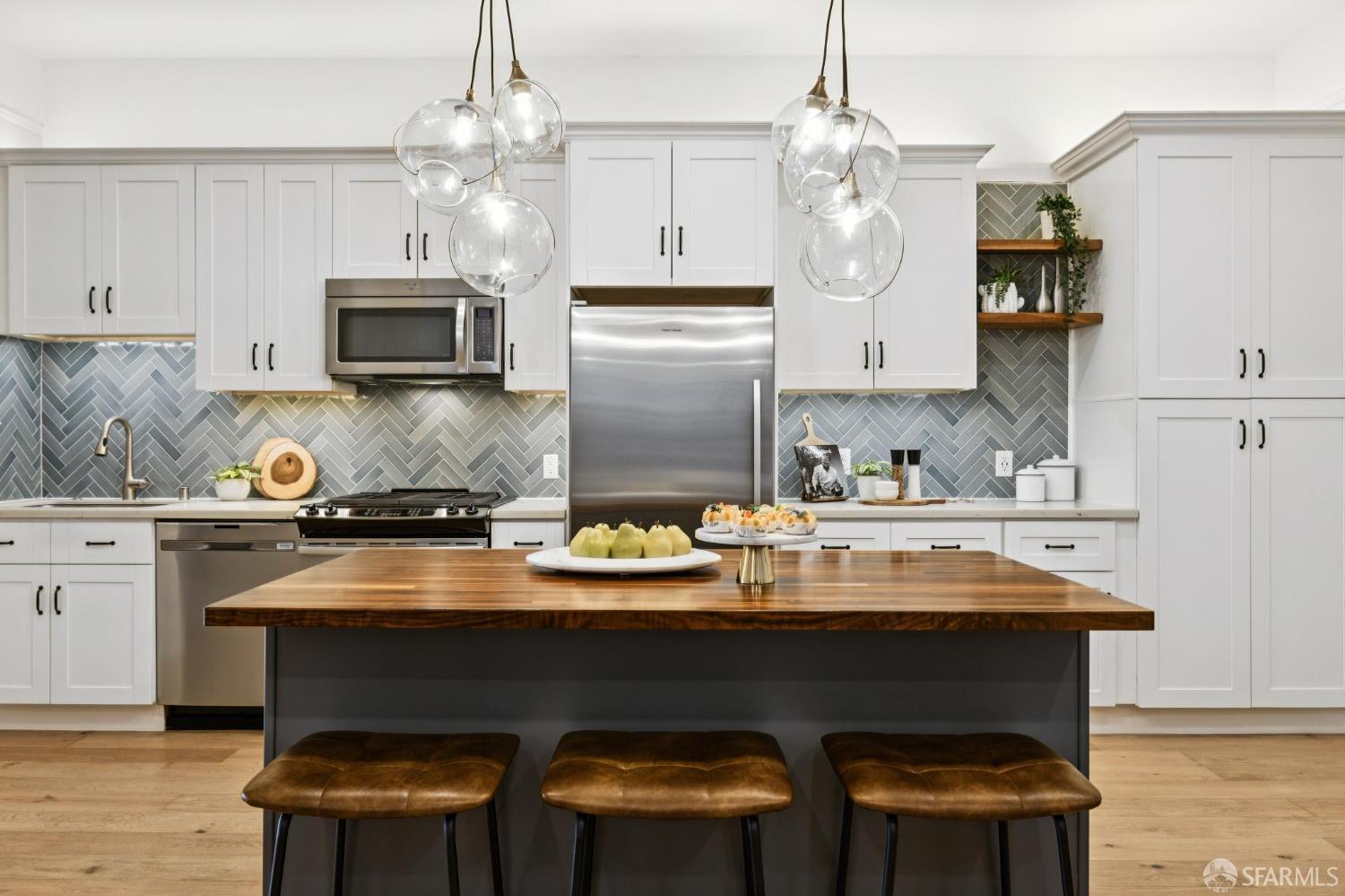 Kitchen with a wood-topped island, three leather stools, and a gray herringbone backsplash.