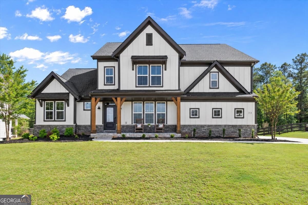 White two-story house with dark gables, timber porch posts, stone foundation, and a broad green lawn.