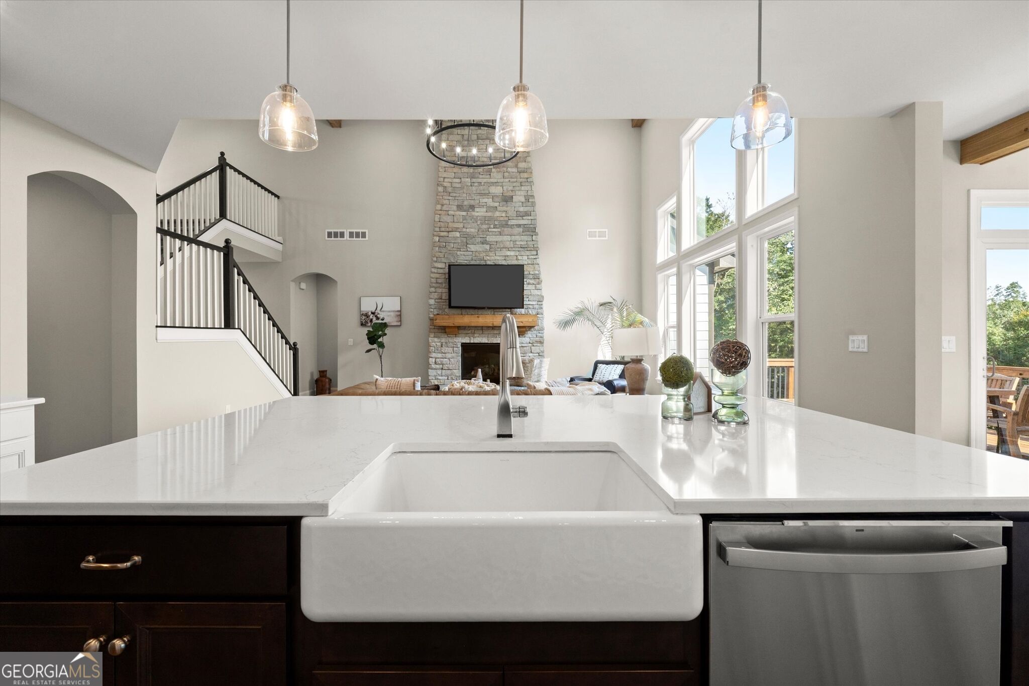 Open-plan kitchen with a white quartz island, farmhouse sink, and stone fireplace beyond.