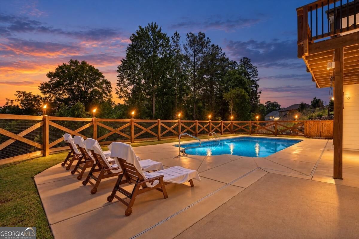 Backyard swimming pool and lounge chairs beside a wooden patio at dusk.