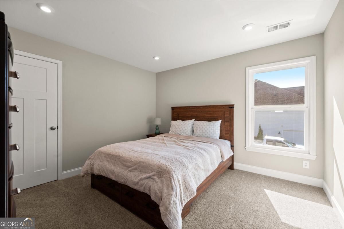 Bedroom with a dark wood bed, pale bedding, beige carpet, and a sunlit window.