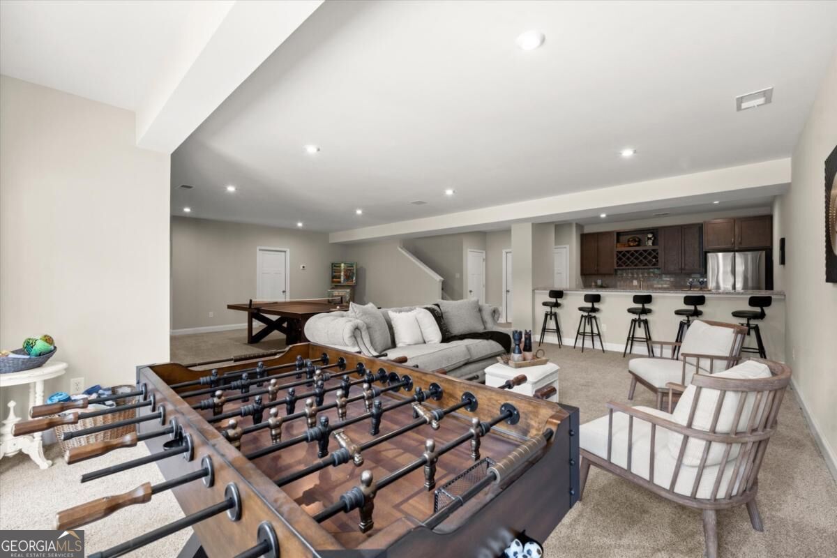Furnished basement recreation room with a foosball table, sofa, game table, and bar seating.