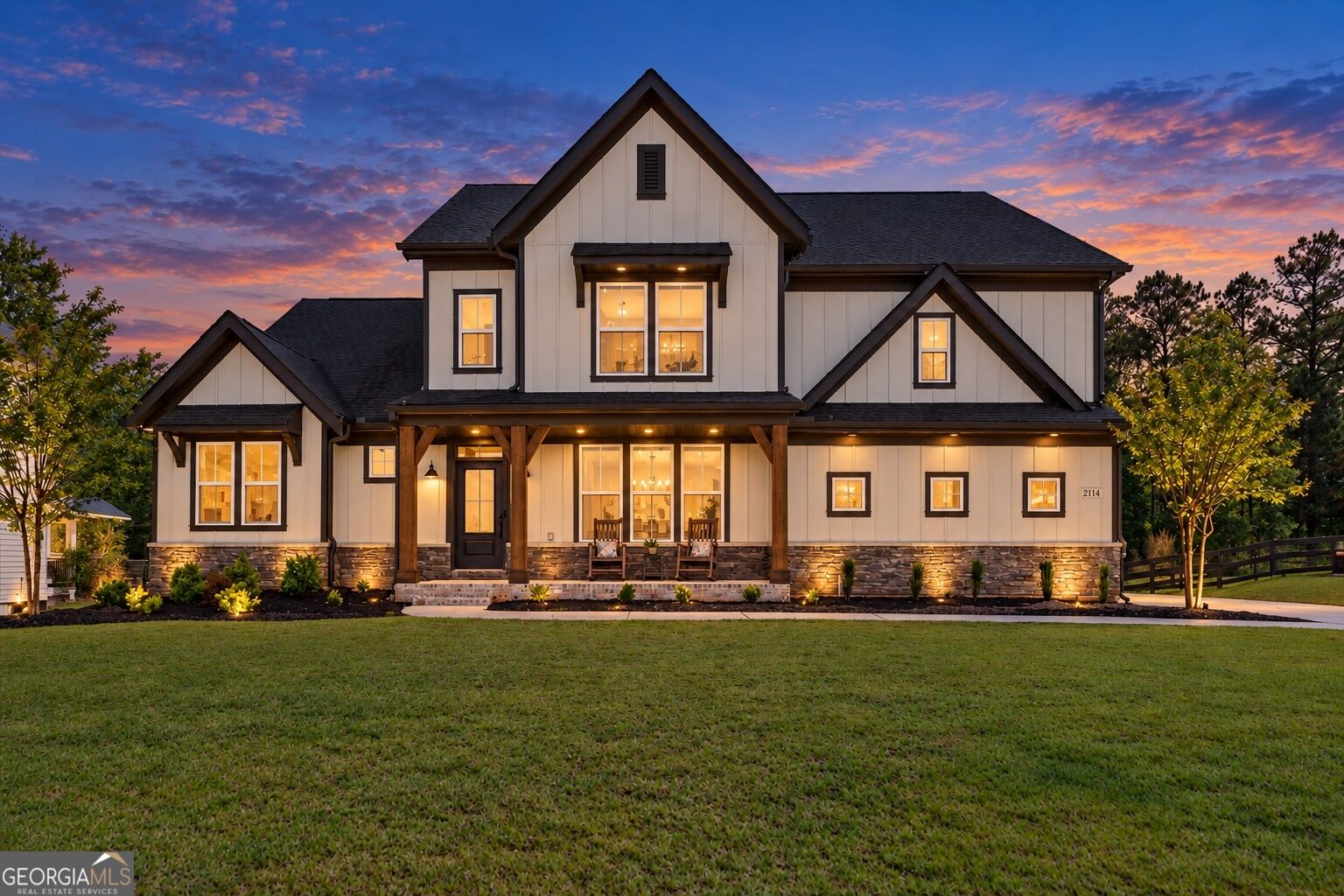 White farmhouse with a covered porch and glowing windows beneath a colorful dusk sky.