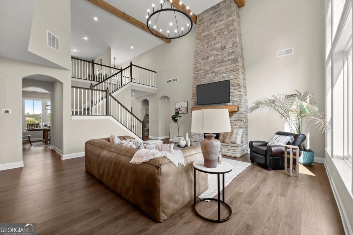 Two-story living room with a tall stone fireplace, exposed ceiling beams, and staircase.