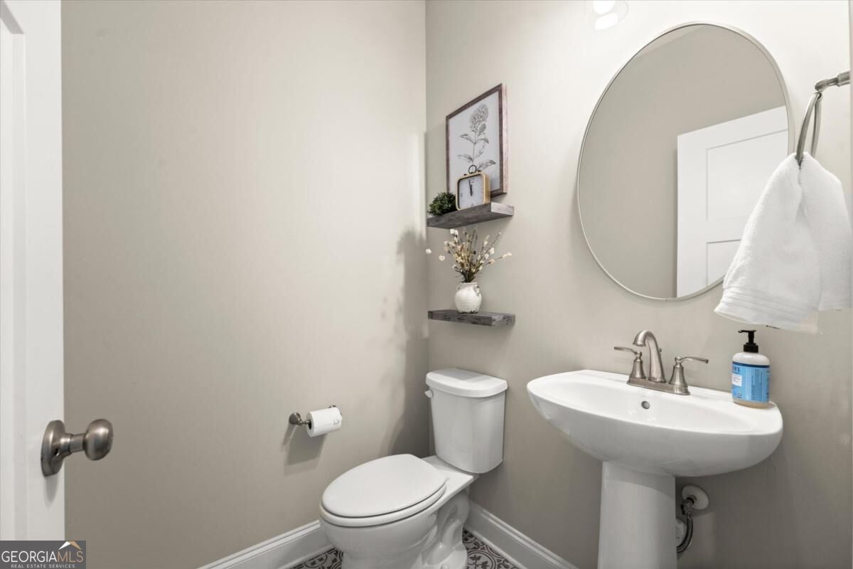 Powder room with a white pedestal sink, large oval mirror, and patterned tile floor.