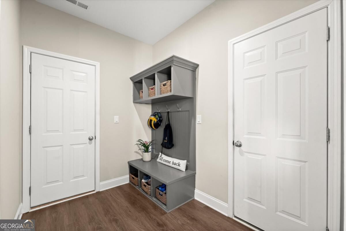 Mudroom with a gray built-in bench, cubbies, baskets, and hooks between two white doors.