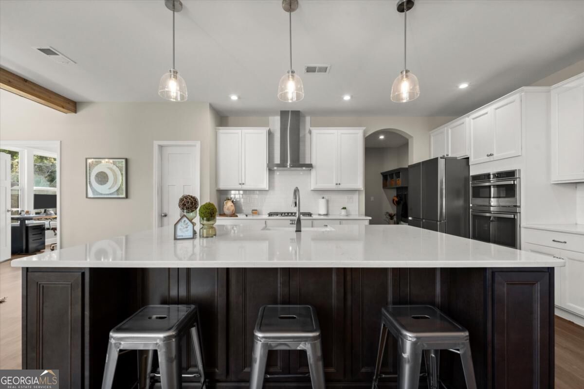 Kitchen with a large dark-paneled island, white countertop, and three metal stools.