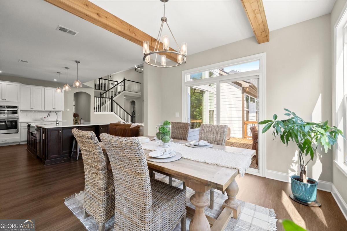 Dining area with woven chairs, exposed wood ceiling beams, and glass doors to a deck.