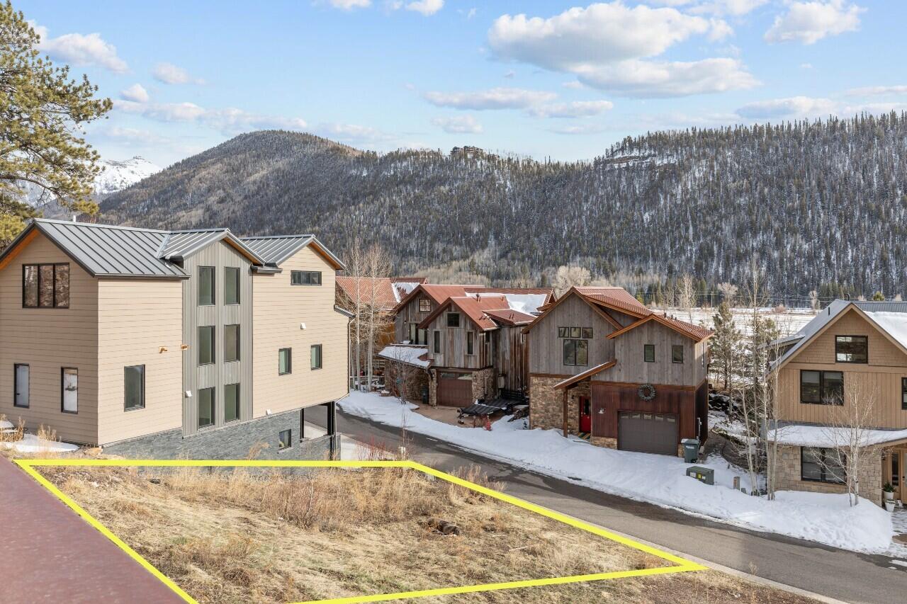 Vacant lot outlined in yellow beside neighboring homes, with snow-dusted mountains behind it.