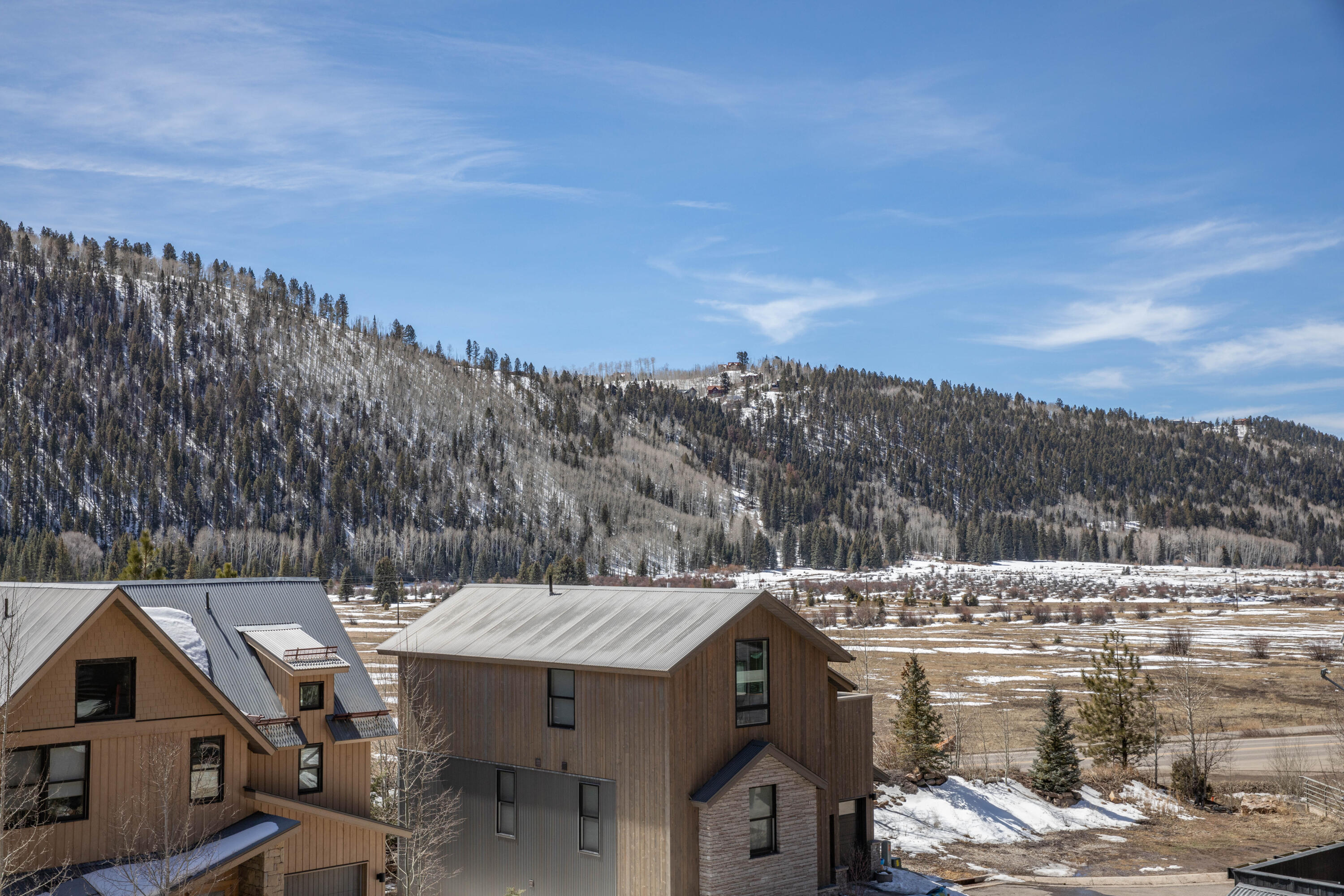 Snow-dusted mountain ridge and open valley viewed over nearby modern homes.