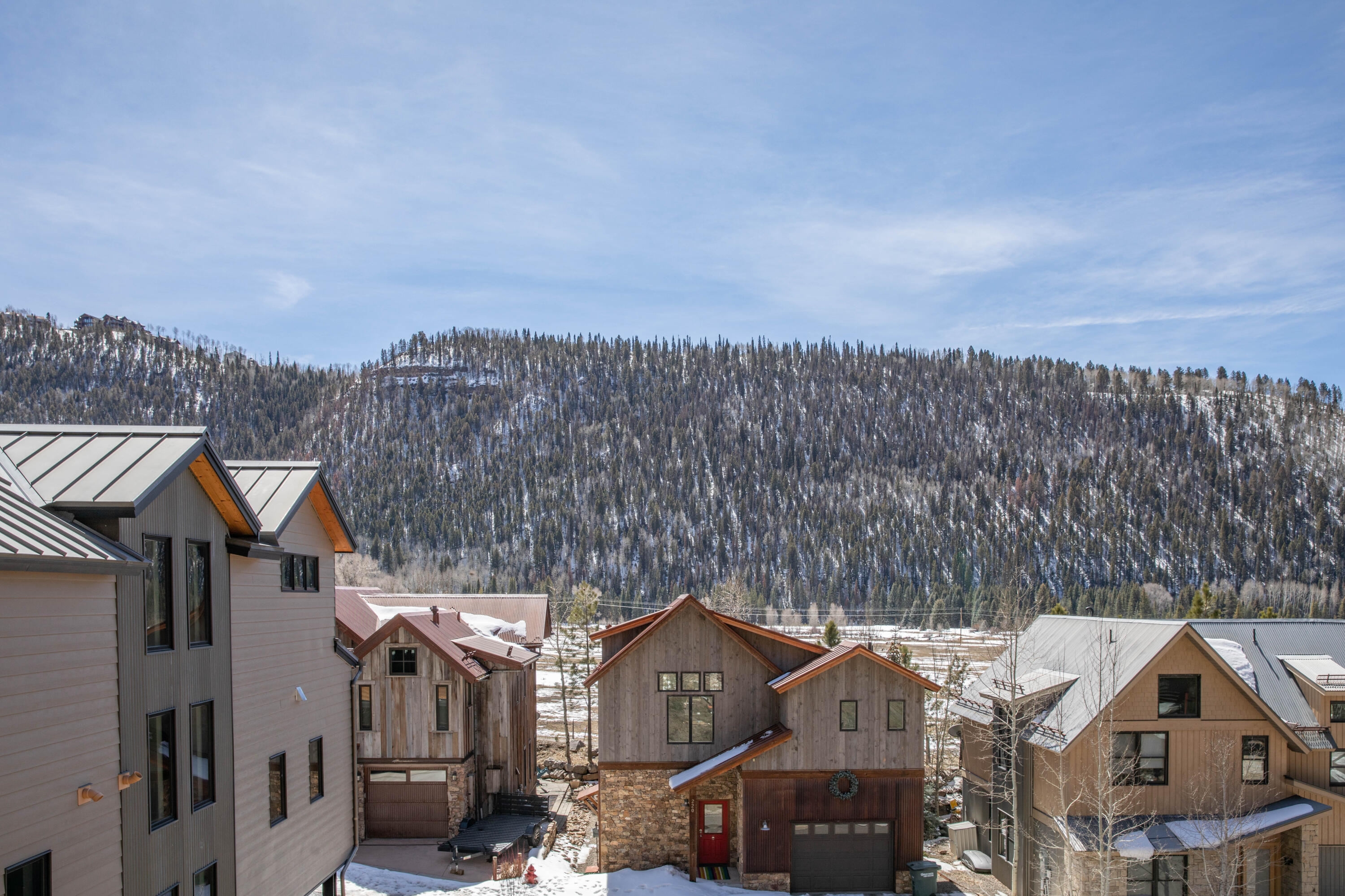 Mountain homes below a snow-dusted forested ridge.