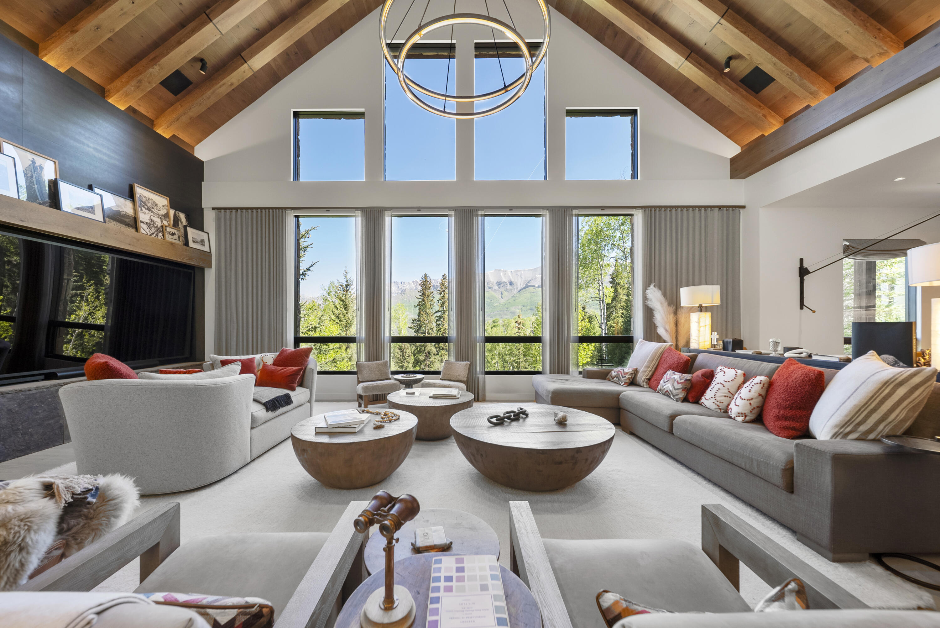 Living room with a vaulted wood ceiling, expansive mountain-view windows, and gray sofas with red accents.