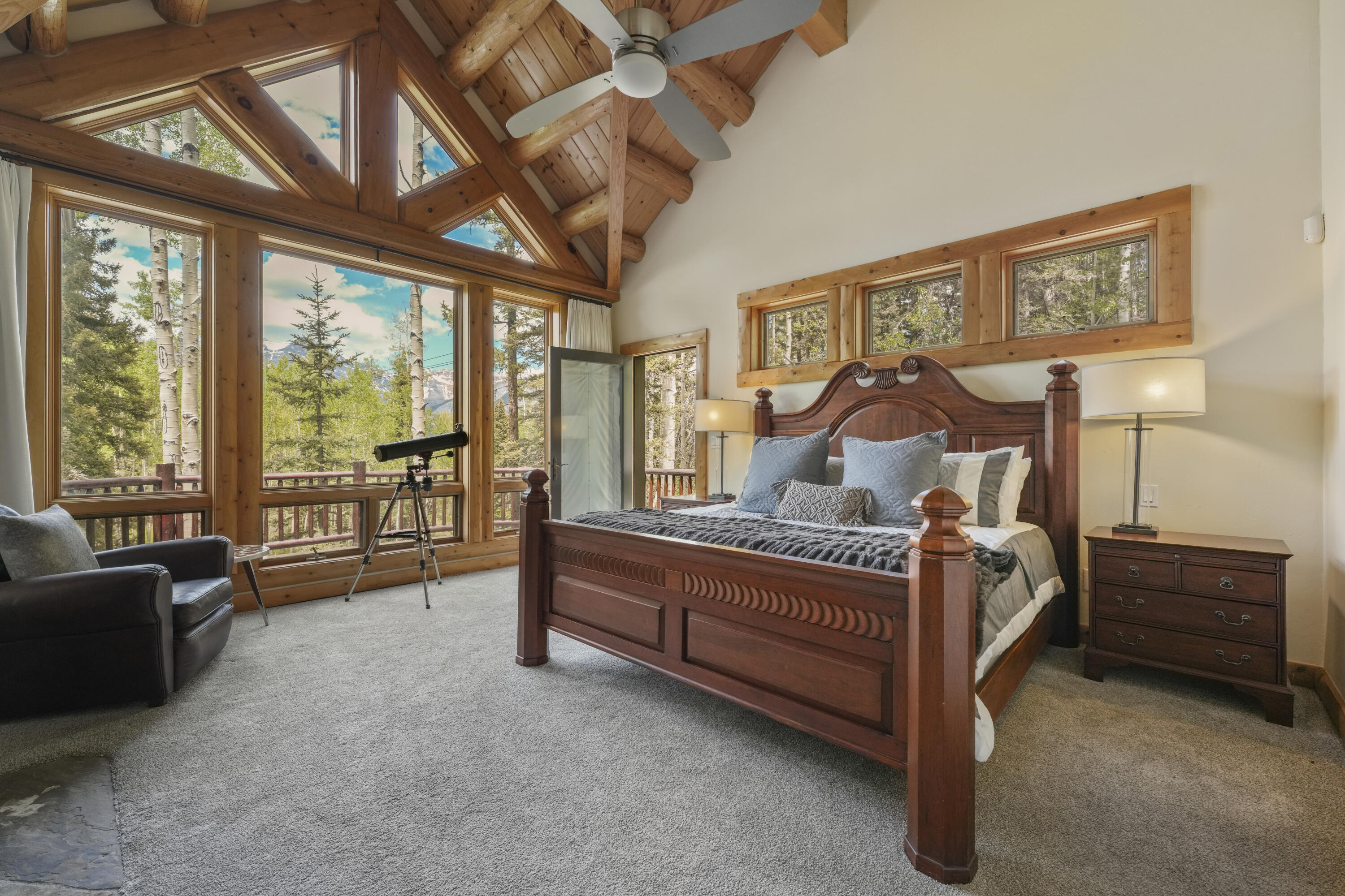 Bedroom with vaulted timber ceiling, carved wooden bed, and large windows overlooking trees and mountains.