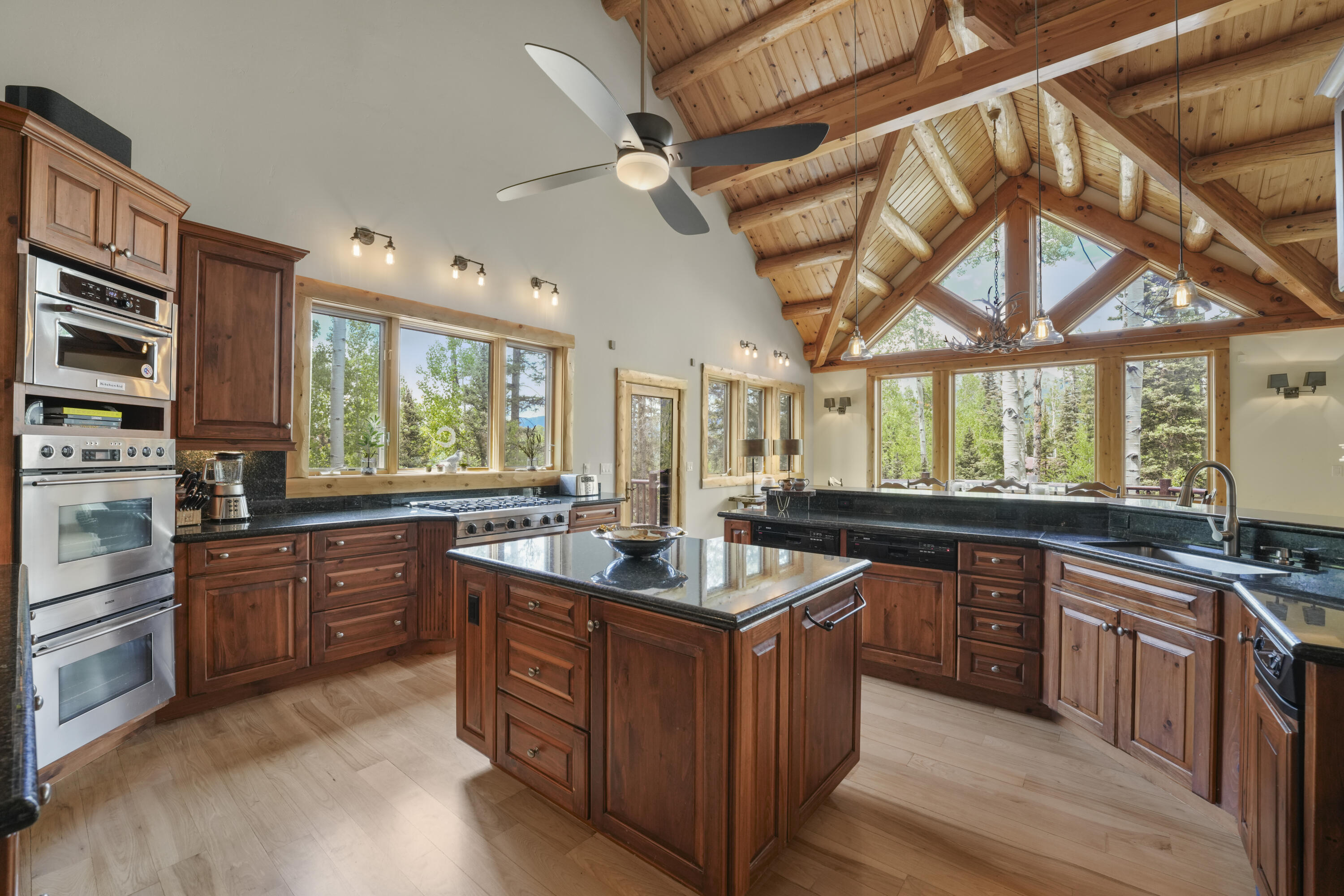 Kitchen with a large island, vaulted timber ceiling, and windows overlooking trees.