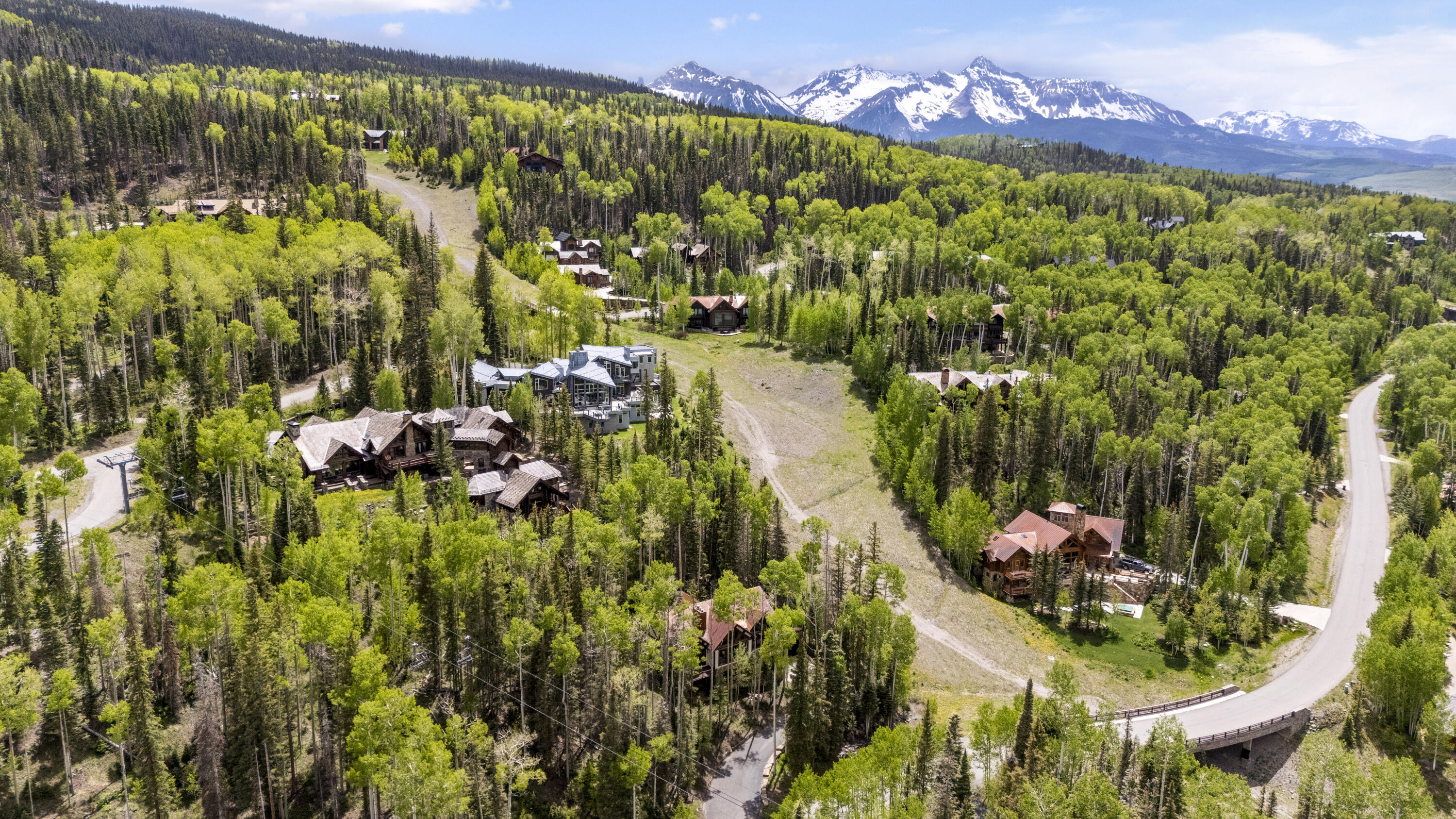 Aerial view of a forested Mountain Village neighborhood, ski run, and snow-capped mountains.