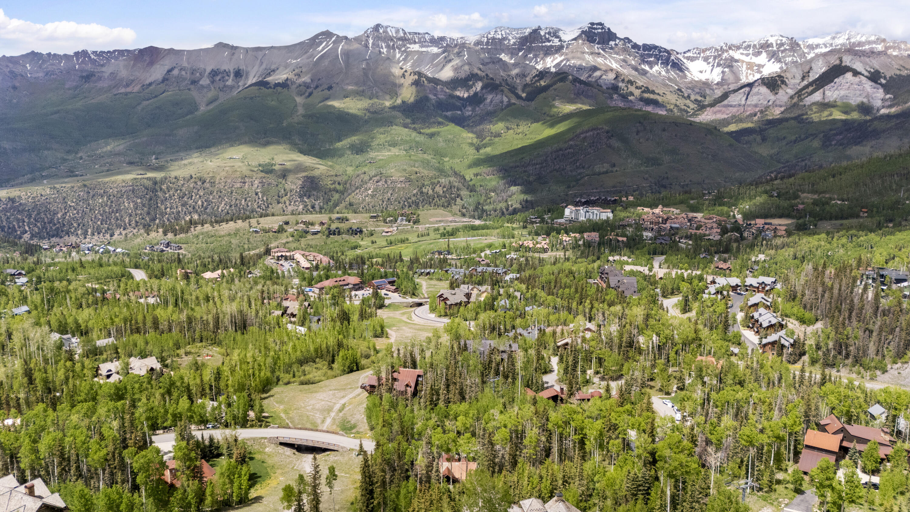 Aerial view of Mountain Village homes among forests, with snow-dusted peaks in the distance.