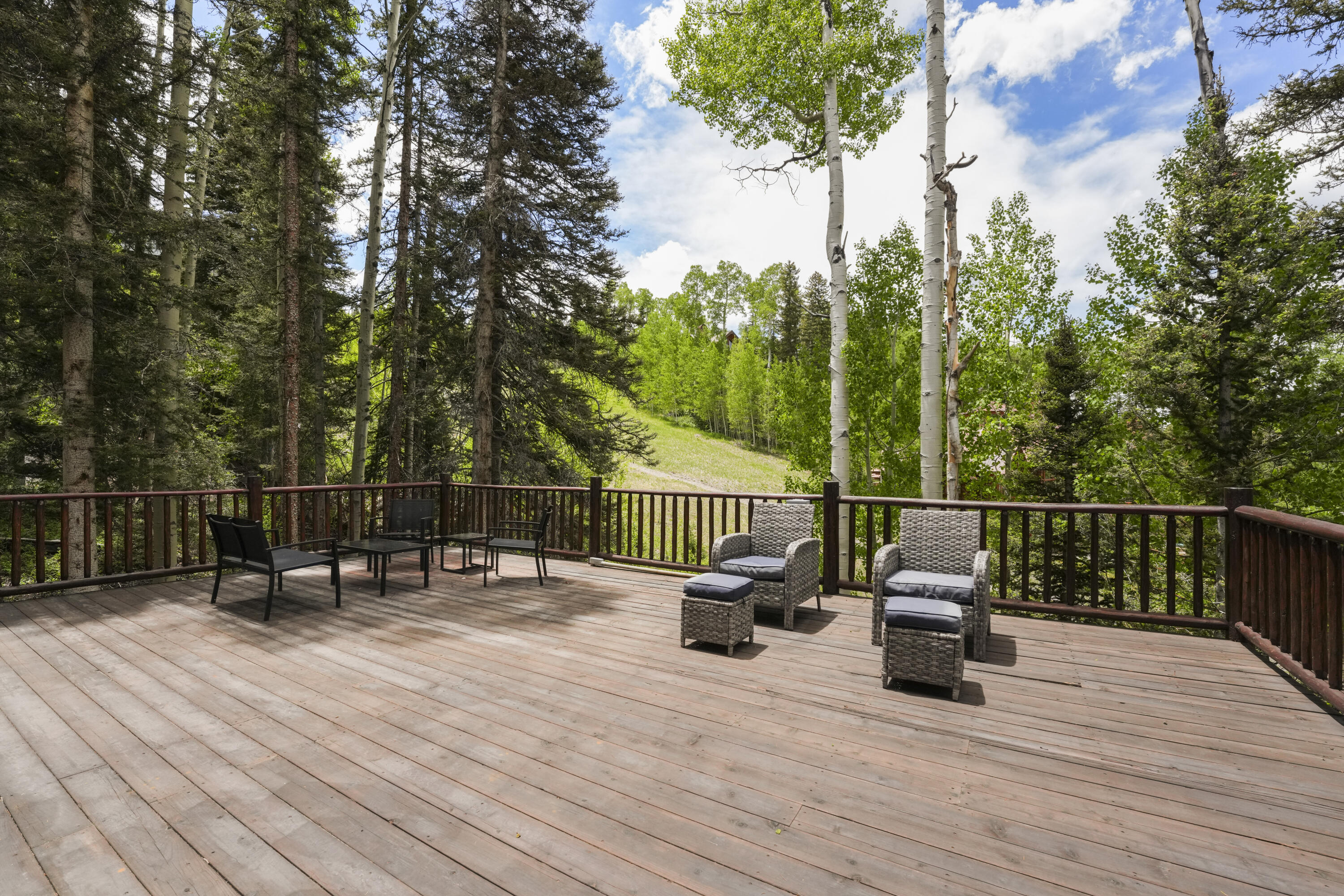 Spacious wood deck with outdoor dining and lounge furniture overlooking a wooded hillside.
